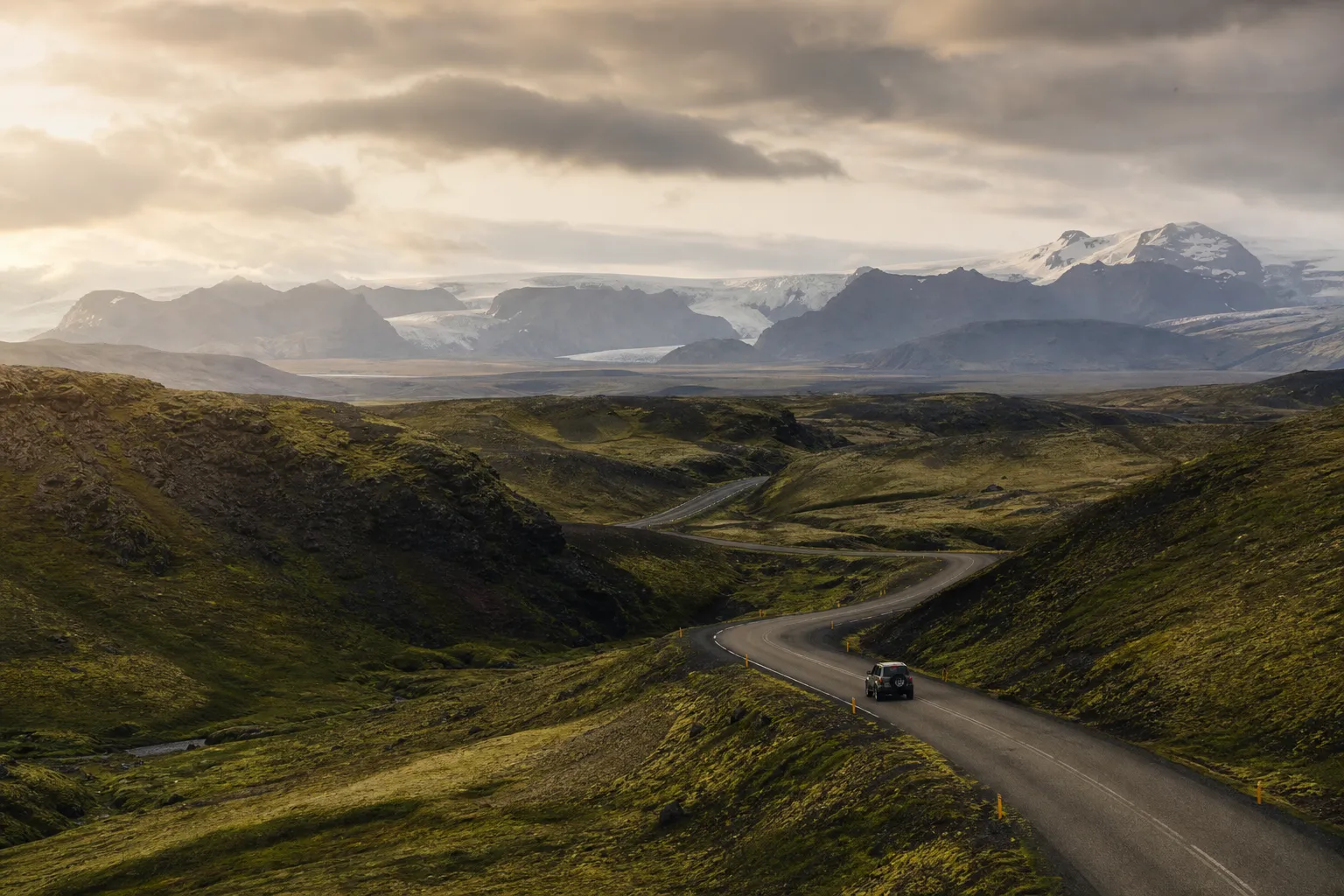 An open road crossing Iceland beneath glaciers and summer clouds